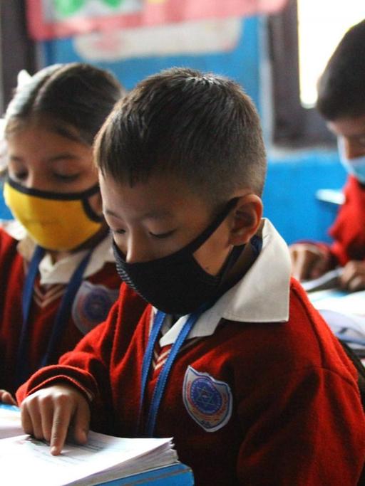 Grundschüler in einer Schule in Nepal sitzen mit Mundschutzen im Klassenzimmer und schreiben in ihre Hefte.