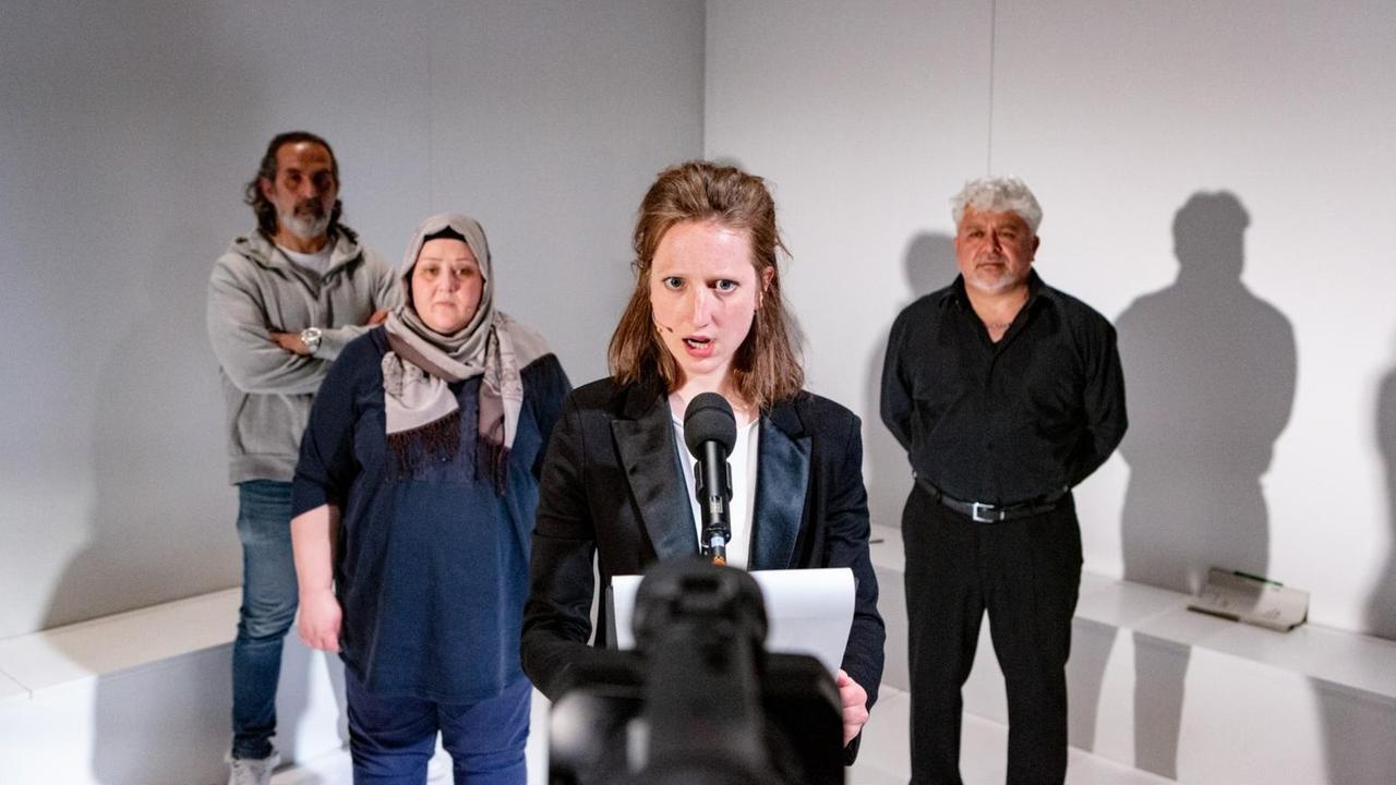 Foto von der Inszenierung: Vier Menschen sprechen auf einer weißen Bühne in eine Kamera. Foto von der Inszenierung: Vier Menschen sprechen auf einer weißen Bühne in eine Kamera.