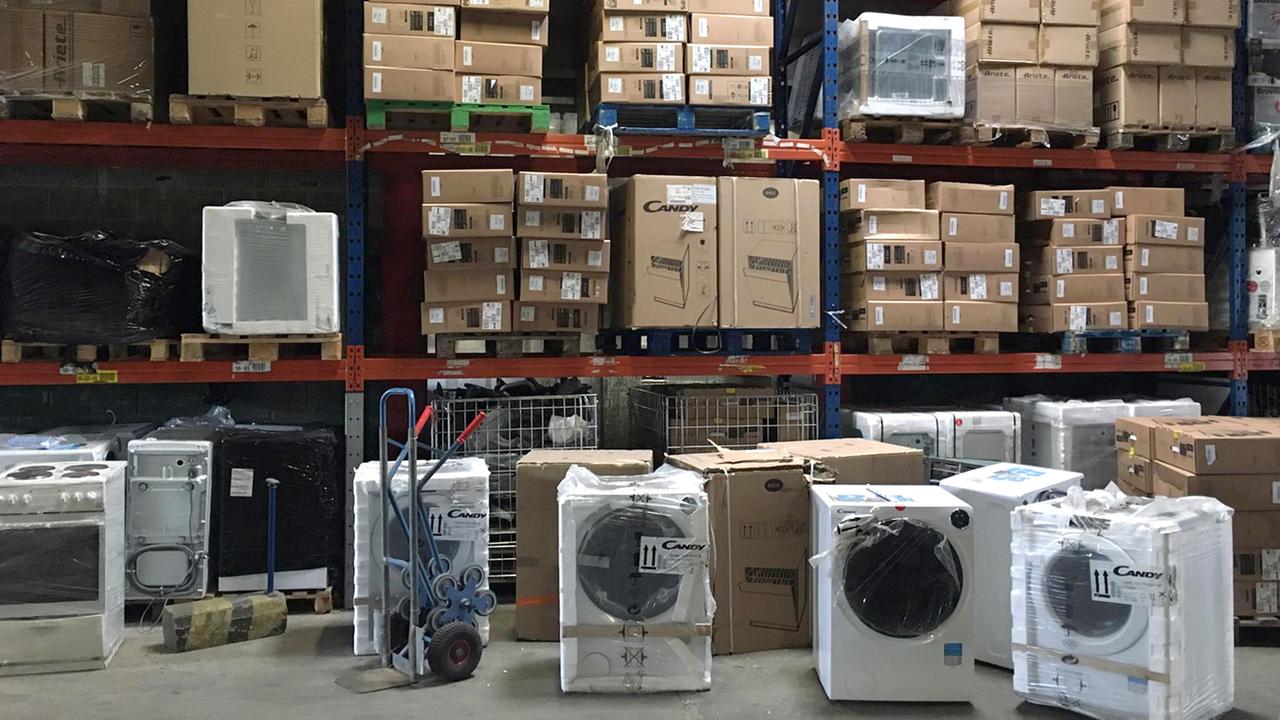 Waschmaschinen und Elektroherde vor und in großen Lagerregalen