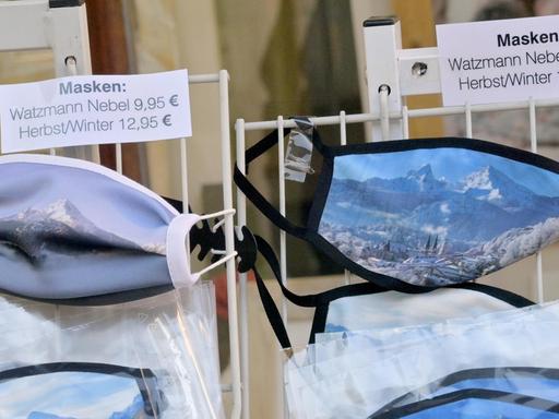 Berchtesgaden: Gesichtsmasken mit einem Motiv vom Watzmann hängen in der Fußgängerzone in einem Geschäft aus.