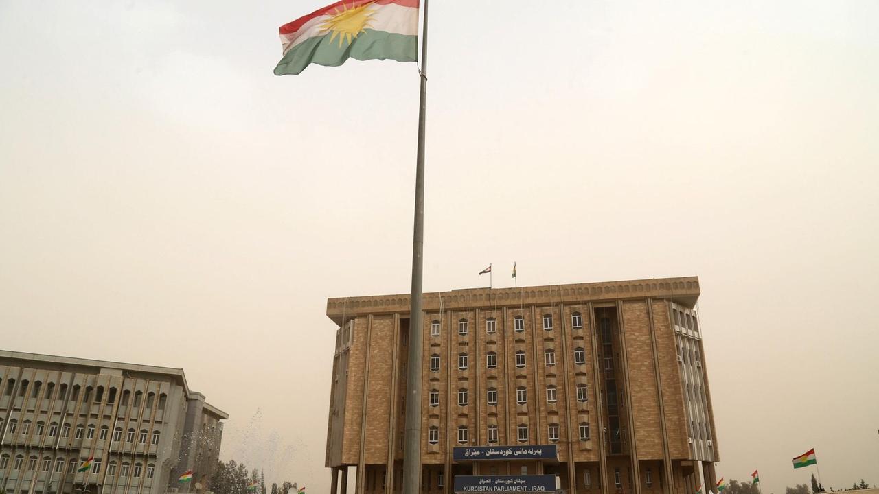 Außenansicht des beigefarbenen Gebäudes mit der Kurdenflagge davor. Außenansicht des beigefarbenen Gebäudes mit der Kurdenflagge davor.