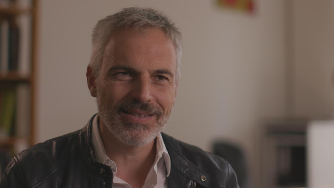 Ein älterer Mann mit Bart sitzt in einem Büro und lächelt. Ein älterer Mann mit Bart sitzt in einem Büro und lächelt.