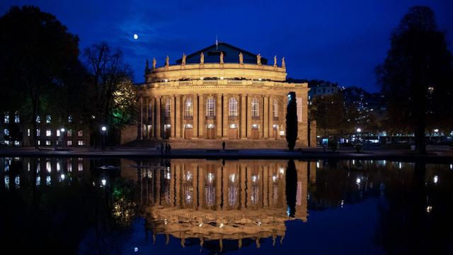 Die beleuchtete Staatsoper Stuttgart und der Mond spiegeln sich nachts im Eckensee.