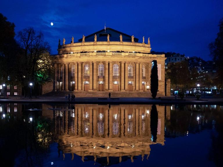Die beleuchtete Staatsoper Stuttgart und der Mond spiegeln sich nachts im Eckensee.