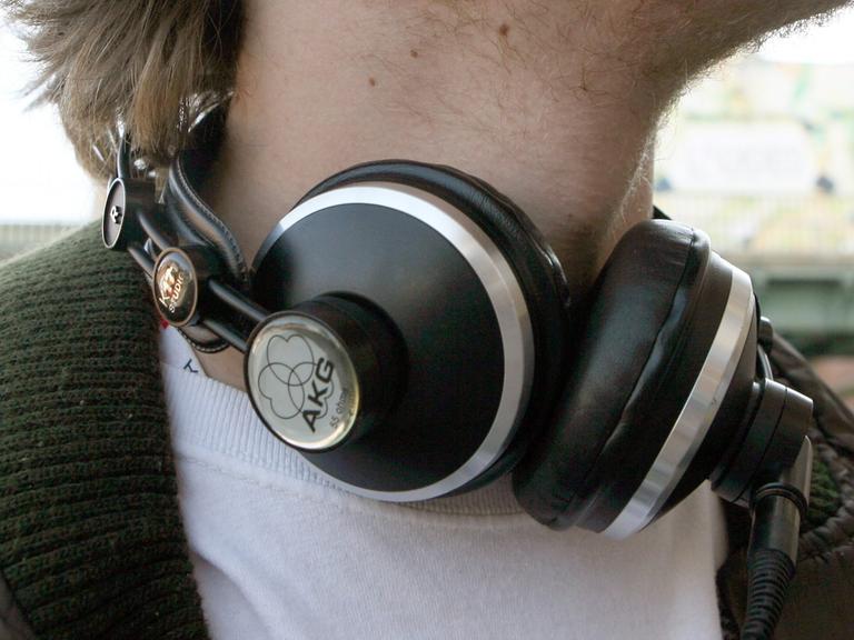 Ein junger Mann trägt große Kopfhörer um den Hals.