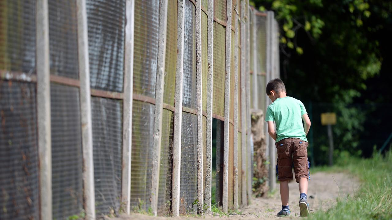Ein Junge geht in Groß-Glienicke (Brandenburg) an einem Rest des Streckmetallzaunes der ehemaligen Berliner Mauer entlang. Ein Junge geht in Groß-Glienicke (Brandenburg) an einem Rest des Streckmetallzaunes der ehemaligen Berliner Mauer entlang.