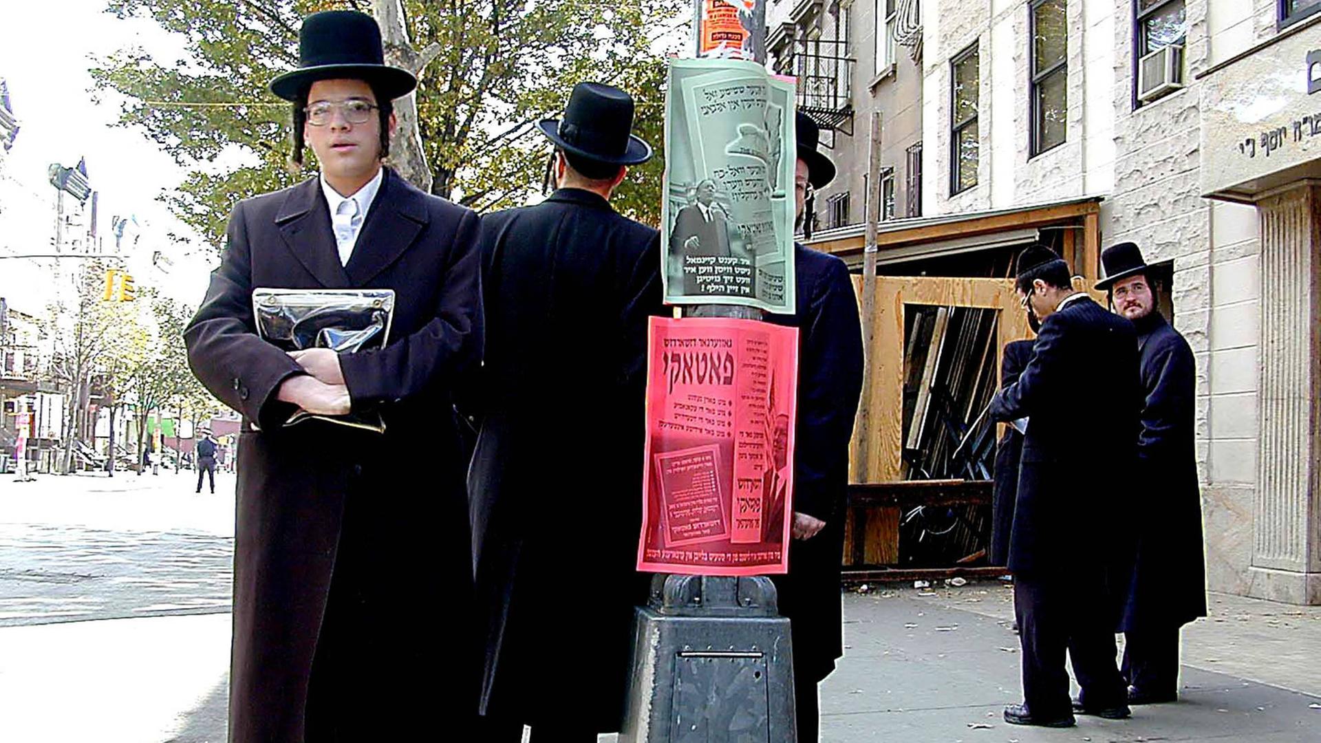 Orthodoxe Juden im New Yorker Stadtteil Williamsburg: Mehrere Männer mit langen schwarzen Mänteln und schwarzen Hüten stehen auf eien Bürgersteig. Orthodoxe Juden im New Yorker Stadtteil Williamsburg: Mehrere Männer mit langen schwarzen Mänteln und schwarzen Hüten stehen auf eien Bürgersteig.