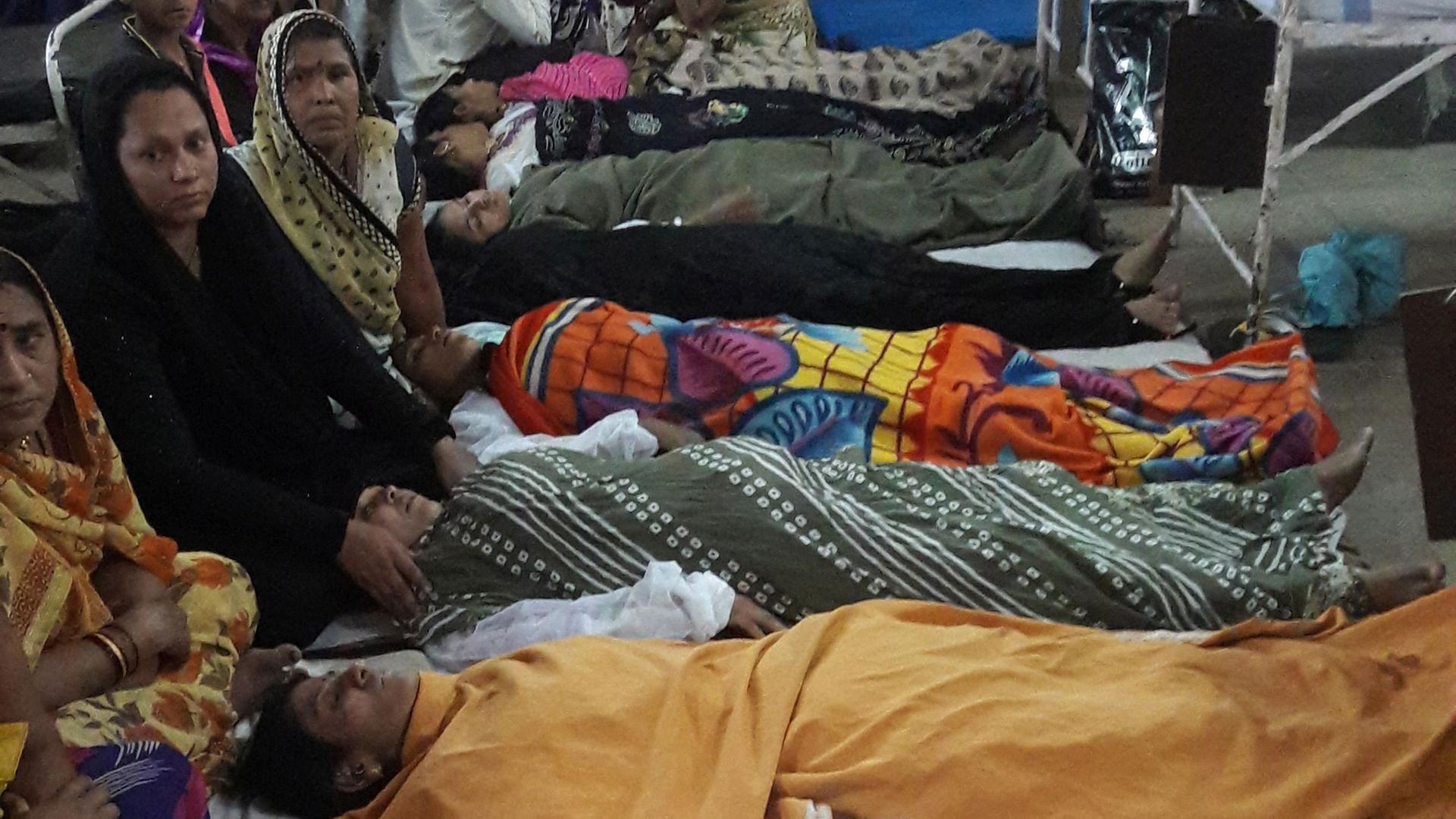 Frauen liegen nach der Operation schlafend auf dem Gang. An ihren Köpfen wachen Verwandte. Frauen liegen nach der Operation schlafend auf dem Gang. An ihren Köpfen wachen Verwandte.