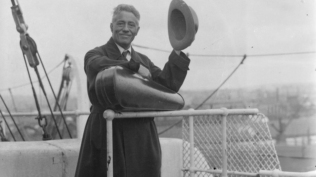 Schwarz-weiß-Foto. Der Geiger Fritz Kreisler 1935 om Southhampton auf der auf dem Weg in die USA. Er steht an der Reling, lüftet seinen Hut, trägt einen dunklen Mantel und hält quer vor sich seinen Geigenkasten. Schwarz-weiß-Foto. Der Geiger Fritz Kreisler 1935 om Southhampton auf der auf dem Weg in die USA. Er steht an der Reling, lüftet seinen Hut, trägt einen dunklen Mantel und hält quer vor sich seinen Geigenkasten.