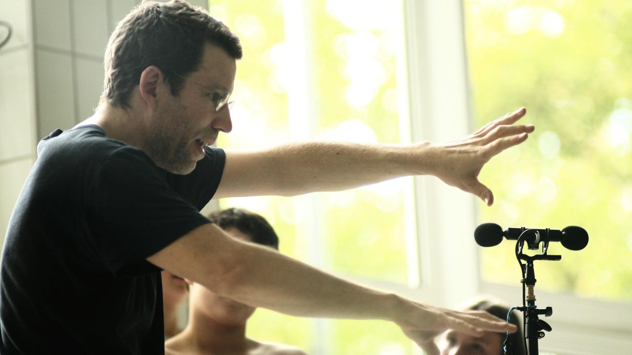 Paul Plamper von der Seite vor einem Mikrofon, die Armei ausgestreckt. Im Hintergrund ein Fenster. Paul Plamper von der Seite vor einem Mikrofon, die Armei ausgestreckt. Im Hintergrund ein Fenster.