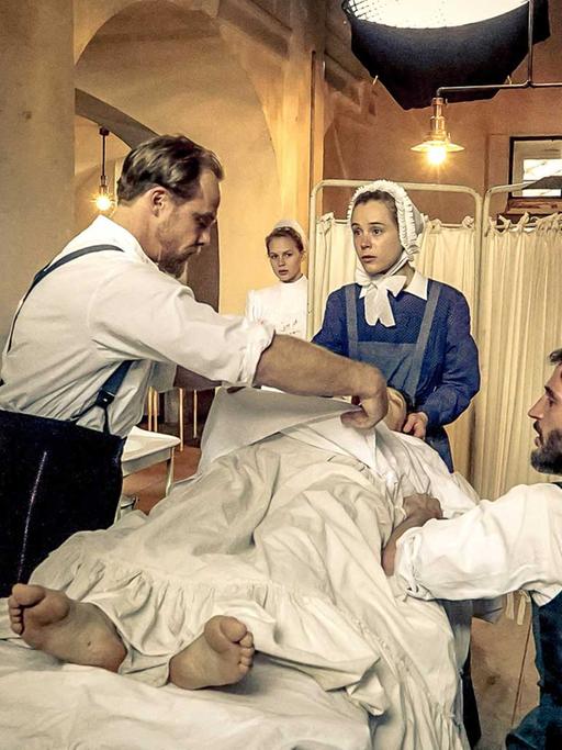 Am Filmset der historischen ARD-Krankenhausserie "Charité" mit sechs Folgen: die Schauspieler Matthias Koeberlin (Rolle Behring, l.), Klara Deutschmann (Rolle Therese; M.) und Christoph Bach (Rolle Ehrlich, 2.v.r.) sowie Kameramann Holly Fink (r.) .