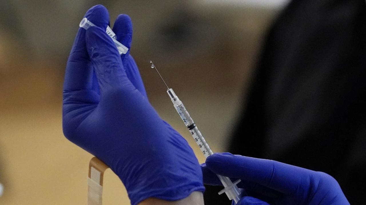 Zwei Hände mit blauen Schutzhandschuhen ziehen eine Spritze zur Impfung auf