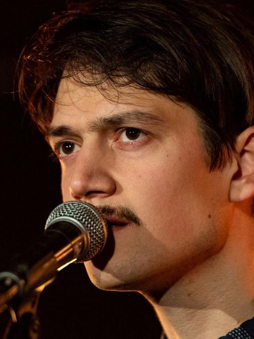 Ein Mann steht auf einer Bühne und singt in ein Mikrofon.