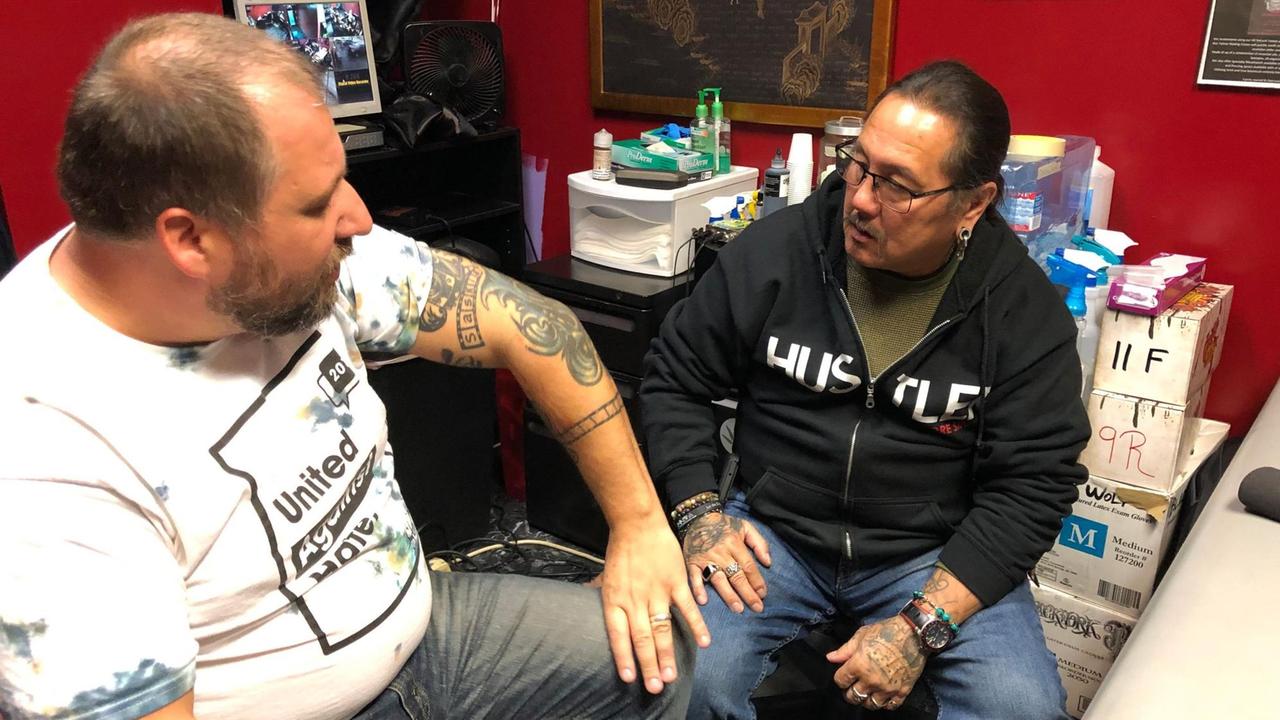 TM Garret Schmid im Tattoo-Studio von Jack Flores in Memphis. Zwei Männer sitze in einem Raum und unterhalten sich. TM Garret Schmid im Tattoo-Studio von Jack Flores in Memphis. Zwei Männer sitze in einem Raum und unterhalten sich.