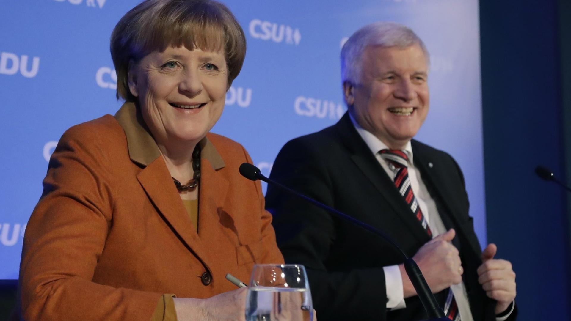Sie sehen Bundeskanzlerin Merkel und CSU-Chef Seehofer auf einer gemeinsamen Pressekonferenz. Beide lachen.