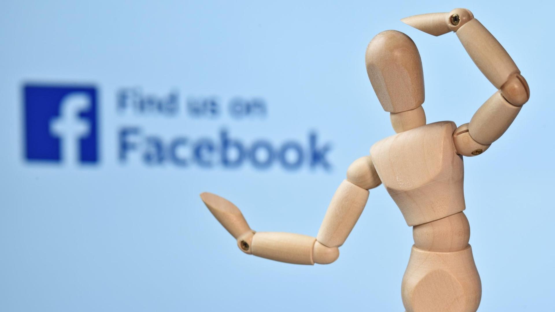 Eine Holzfigur vor dem Logo von Facebook. Eine Holzfigur vor dem Logo von Facebook.