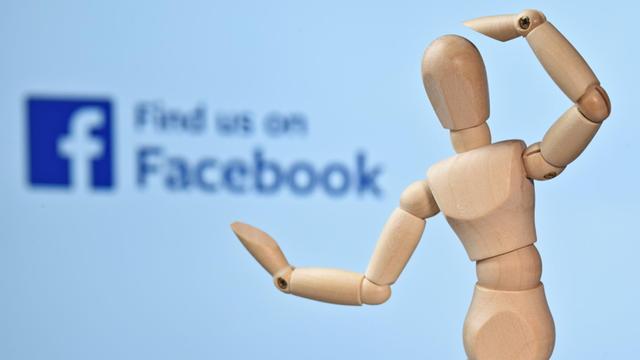 Eine Holzfigur vor dem Logo von Facebook.