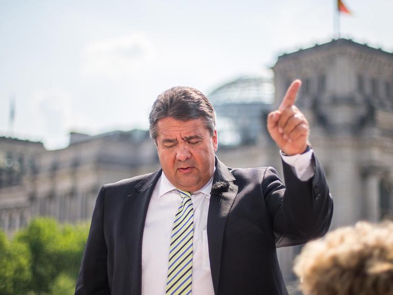 Bundeswirtschaftsminister Sigmar Gabriel (SPD) steht am 27.07.2014 auf der Terrasse des Marie-Elisabeth-Lüders-Hauses in Berlin während des Sommerinterviews für die ARD-Sendung "Bericht aus Berlin" und deutet mit dem Zeigefinger. Im Hintergrund der Reichstag.