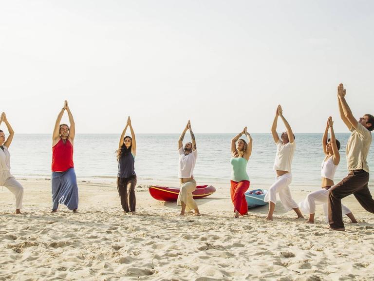 Eine Gruppe Menschen macht Yoga am Strand.