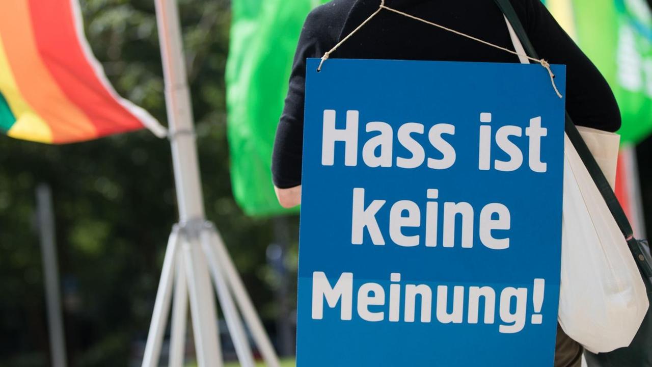 Eine Frau steht mit einem Plakat mit der Aufschrift "Hass ist keine Meinung" an ihrem Rücken.