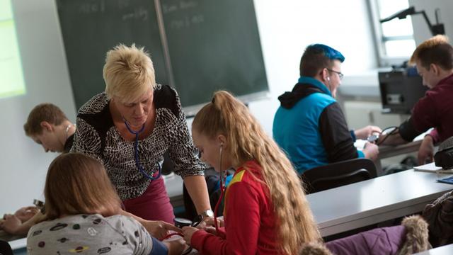 Die Lehrerin für Altenpflege am Institut für Weiterbildung in der Kranken- und Altenpflege zeigt in Magdeburg in einem Klassenraum zwei Schülerinnen den Umgang mit einem Blutdruckmessgerät