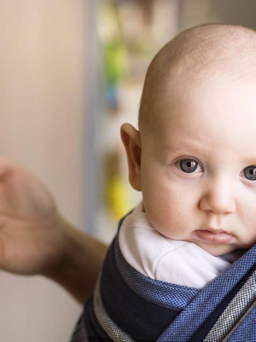 Ein Vater trägt ein Baby an der Brust und schaut dabei auf sein Smartphone