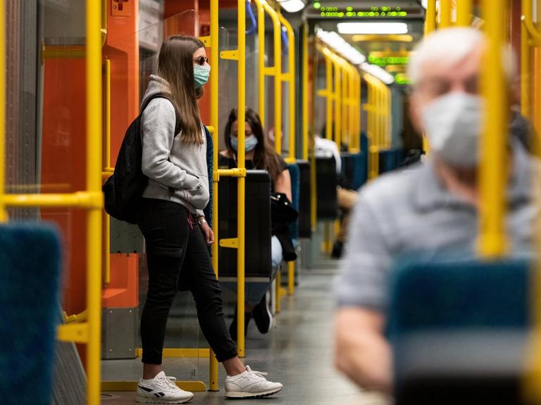 Blick in eine Bahn: Dort sitzen Menschen mit Masken vor dem Gesicht.