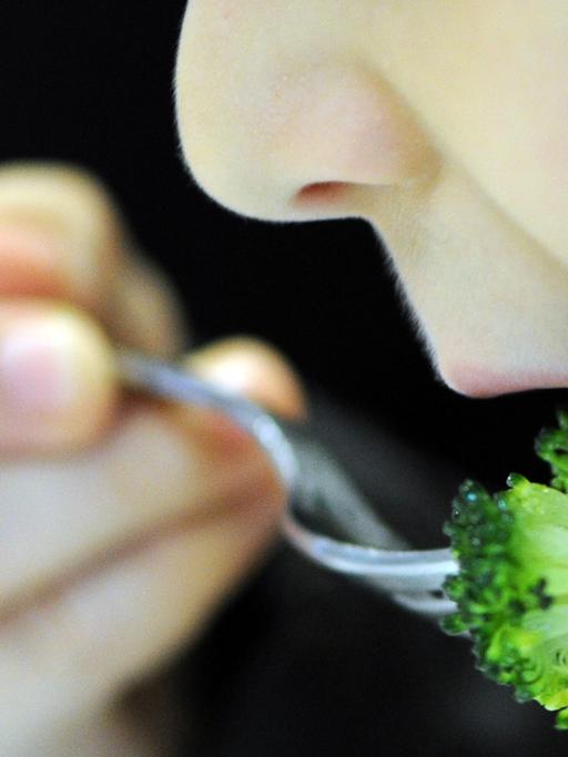 Ein Kind schiebt sich mit einer Gabel ein Stück Brokkoli in den Mund.