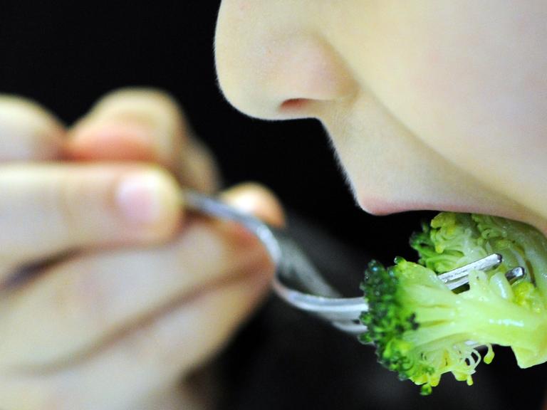 Ein Kind schiebt sich mit einer Gabel ein Stück Brokkoli in den Mund.