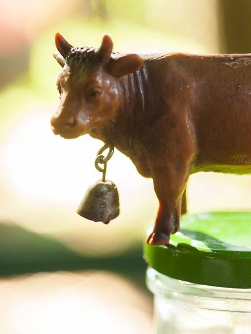 Eine Spielzeugkuh mit einer Kuhglocke steht auf eine Milchflasche mit frischer Bio-Rohmilch.