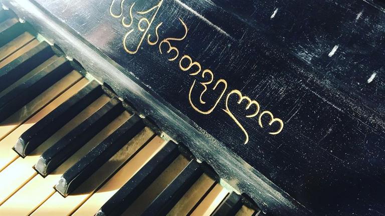 Blick auf alte Klaviertasten, über denen ein georgischer Schriftzug zu sehen ist. Blick auf alte Klaviertasten, über denen ein georgischer Schriftzug zu sehen ist.