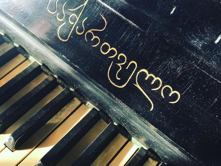 Blick auf alte Klaviertasten, über denen ein georgischer Schriftzug zu sehen ist.
