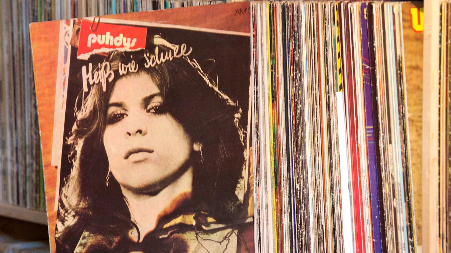 Aus einem Regal mit zahlreichen Schallplatten wurde die LP "Heiß wie Schnee" von den Puhdys herausgezogen. Auf dem Cover ist das Porträt einer Frau zu sehen.