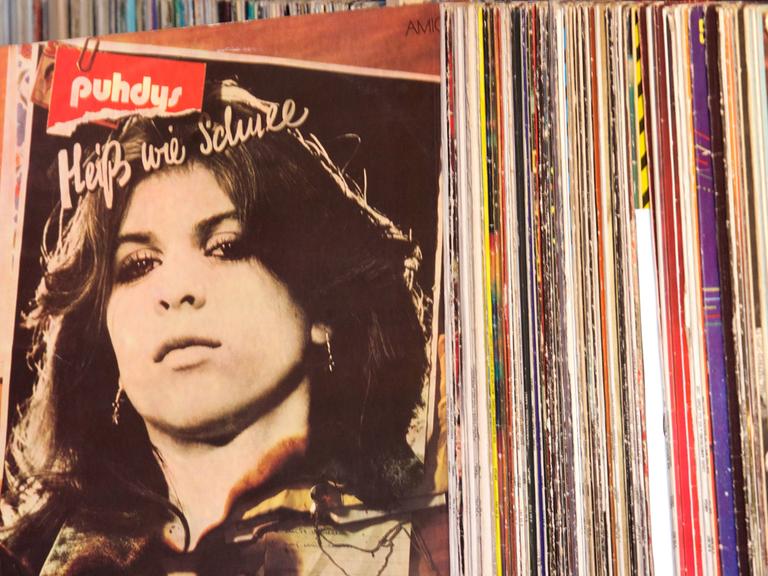 Aus einem Regal mit zahlreichen Schallplatten wurde die LP "Heiß wie Schnee" von den Puhdys herausgezogen. Auf dem Cover ist das Porträt einer Frau zu sehen.