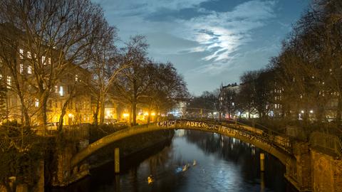 Eine Gruppe Schwäne schwimmt auf dem Landwehrkanal in Berlin in Richtung Kottbusser-Brücke, während das Mondlicht sich im Wasser spiegelt.