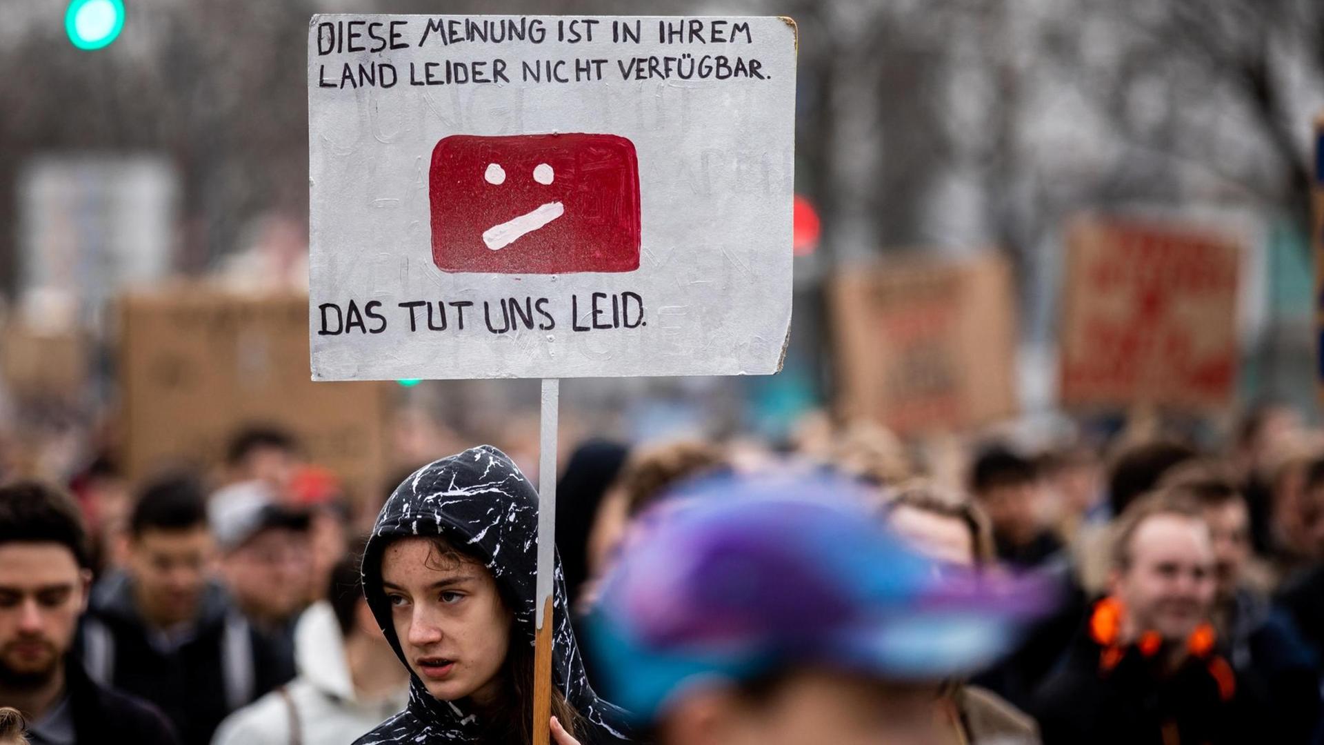 Demonstrierende mit Demoschild und der Aufschrift "Diese Meinung ist in Ihrem Land leider nicht verfügbar. Das tut uns Leid" Demonstrierende mit Demoschild und der Aufschrift "Diese Meinung ist in Ihrem Land leider nicht verfügbar. Das tut uns Leid"