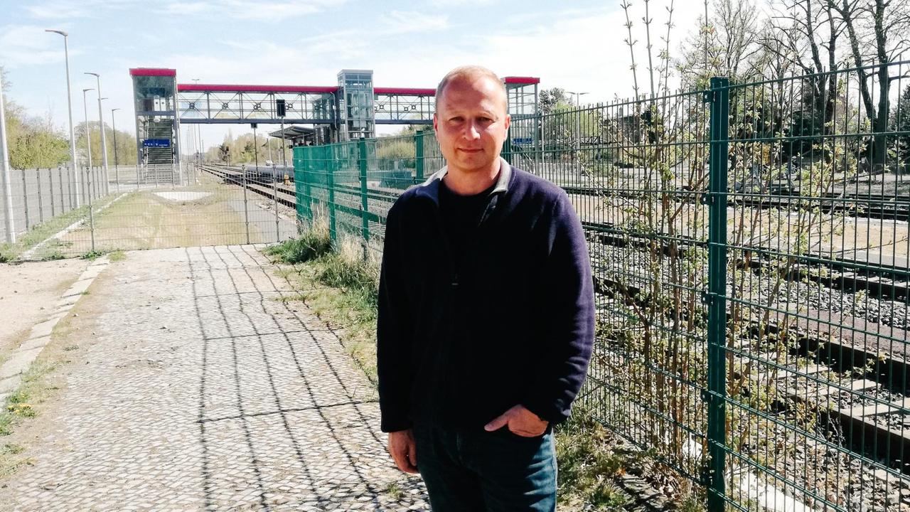 Marcus Siegert, Stadtverordneter von Velten für die Wählervereinigung Pro Velten, steht vor einem abgezäunten Bahngleis.