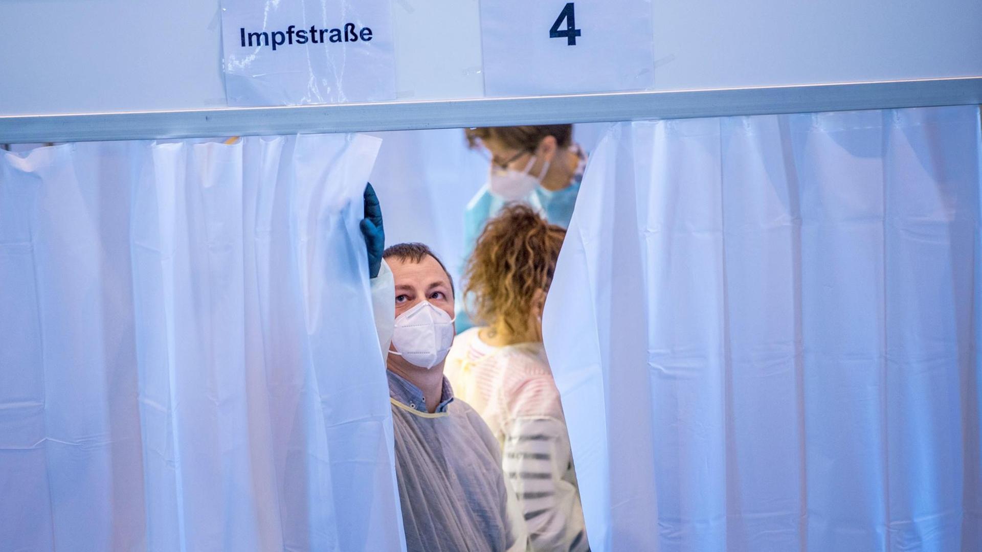 Ein Mitarbeiter schließt im Impfzentrum den Vorhang einer Kabine, in der gegen das Coronavirus geimpft wird.