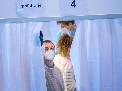 Ein Mitarbeiter schließt im Impfzentrum den Vorhang einer Kabine, in der gegen das Coronavirus geimpft wird.