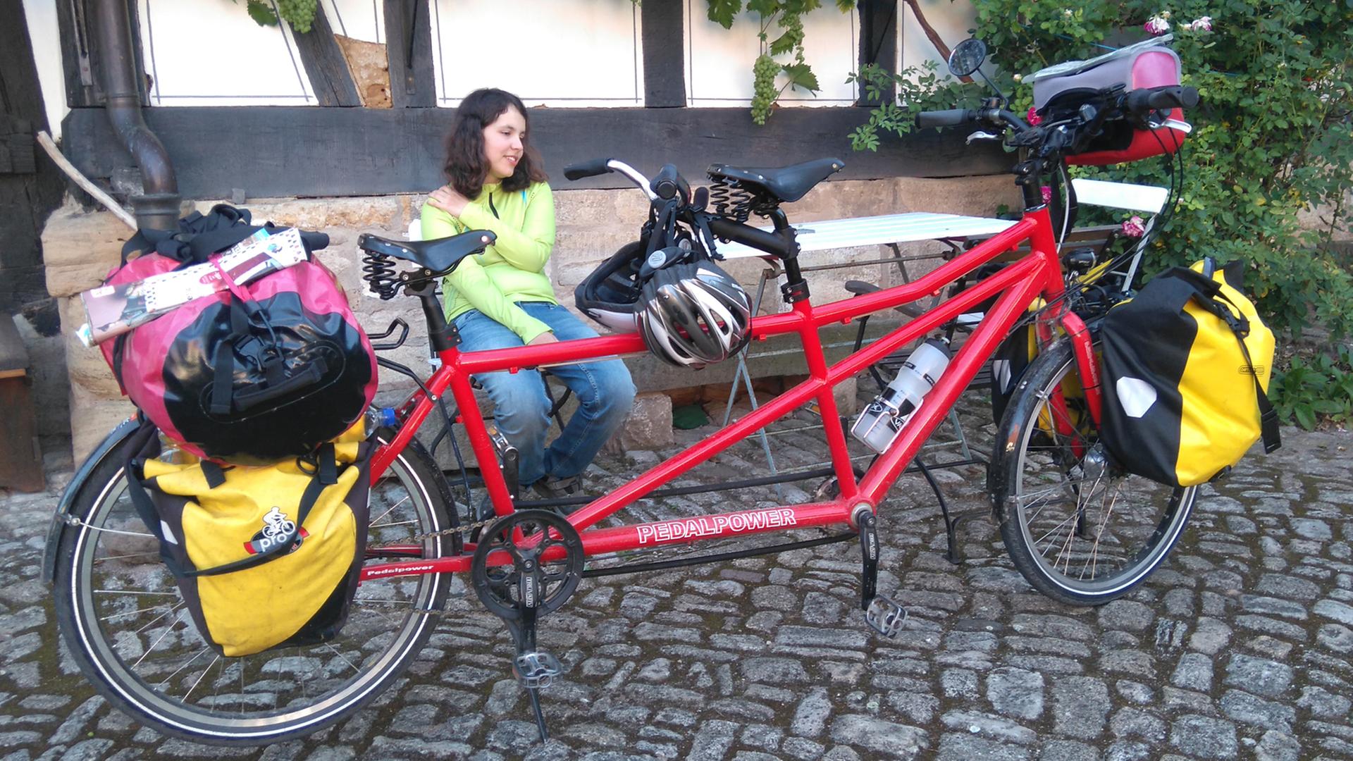 Maral Schäfer sitzt auf einer Bank vor einem Fachwerkhaus, vor ihr das rote Tandem. Maral Schäfer sitzt auf einer Bank vor einem Fachwerkhaus, vor ihr das rote Tandem.