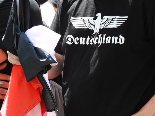 Ein Teilnehmer einer Demonstration von Rechtsextremen hält eine schwarz-weiß-rote Fahne in der Hand und trägt ein schwarzes T-Shirt mit der Aufschrift "Deutschland".