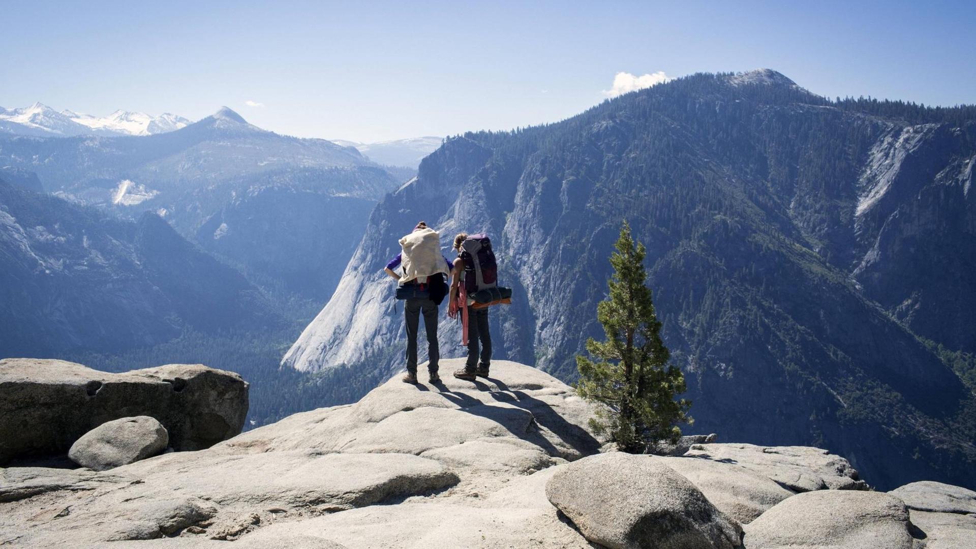 Zwei Wanderer blicken über Berge im Yosemite-Nationalpark in den USA.