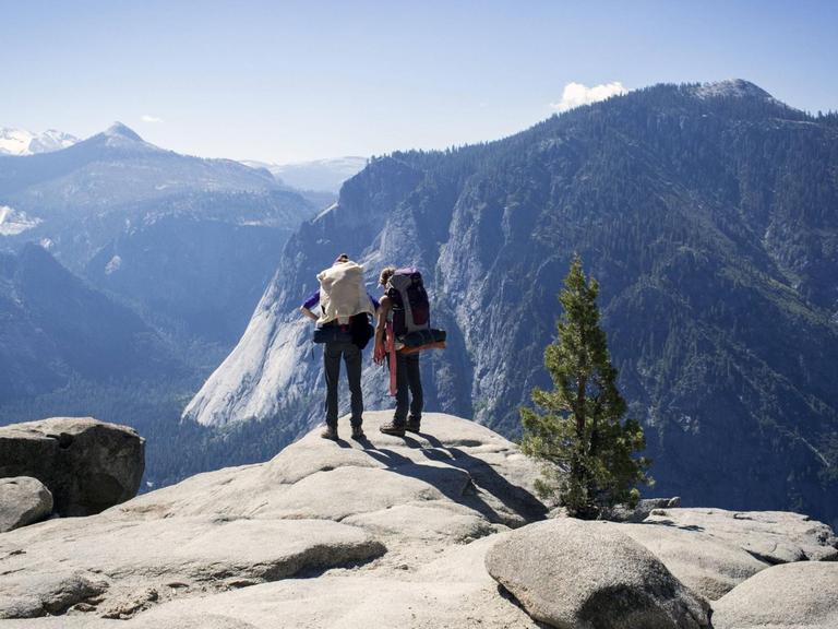 Zwei Wanderer blicken über Berge im Yosemite-Nationalpark in den USA.