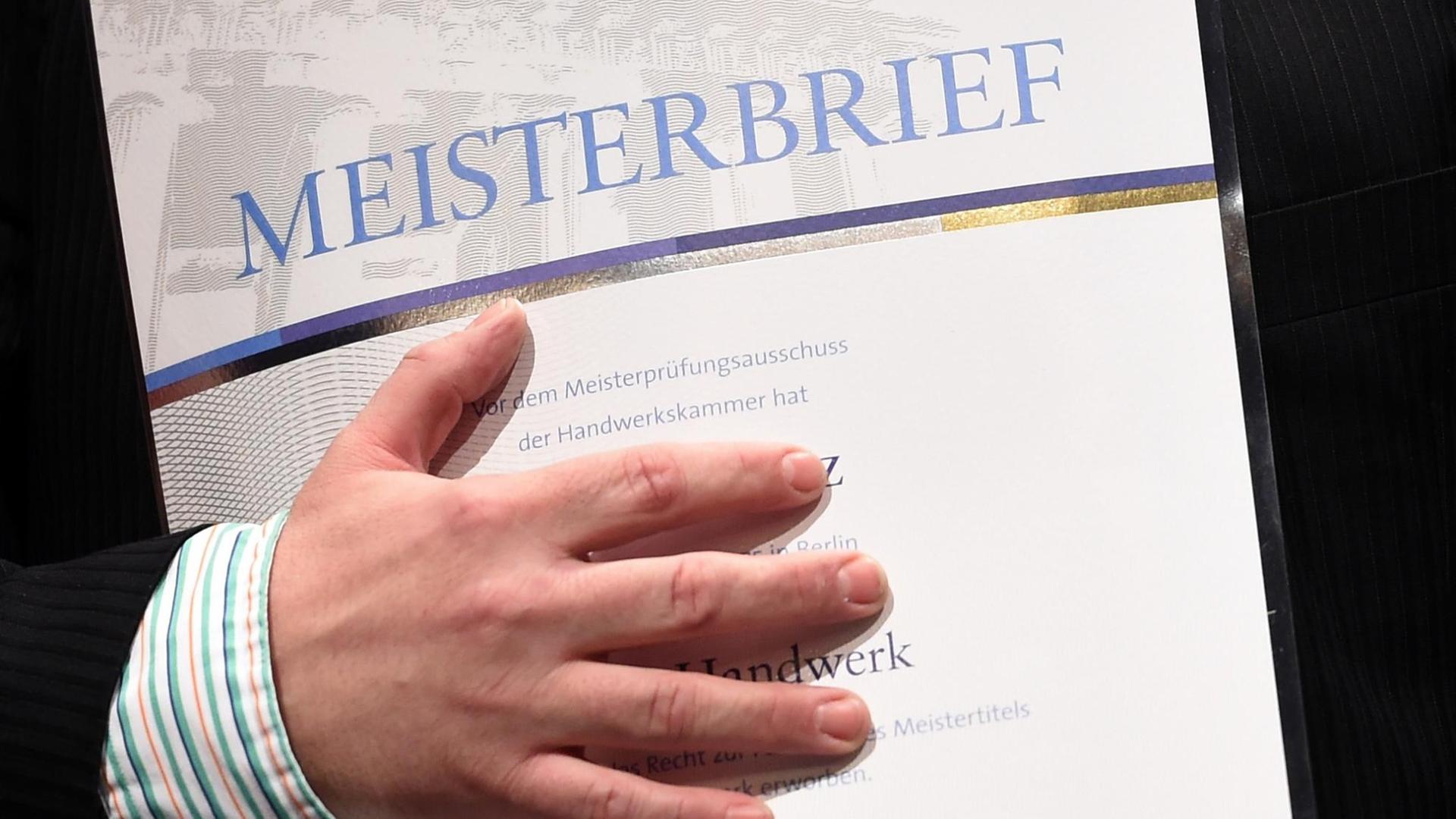 Ein junger Mann hält bei einer Meisterfeier in Erfurt seinen Meisterbrief in der Hand.
