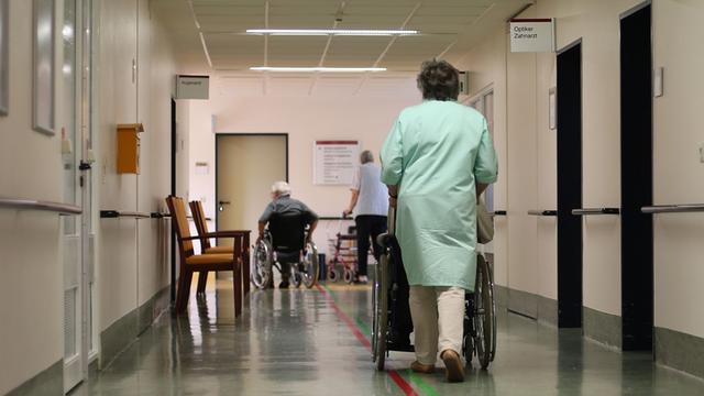 Eine Pflegerin schiebt einen Rollstuhl über einen Flur.