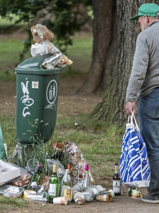 Farbfoto, ein alter Mann sammelt Flaschen vor einem städtischen Müllbehälter