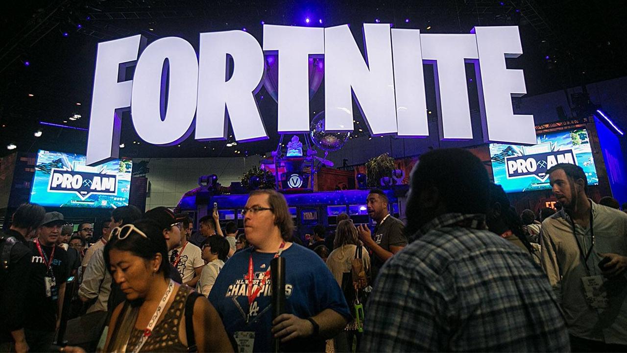 Verschiedene Leute stehen auf einem Messegelände unter einem Fortnite-Schild Verschiedene Leute stehen auf einem Messegelände unter einem Fortnite-Schild