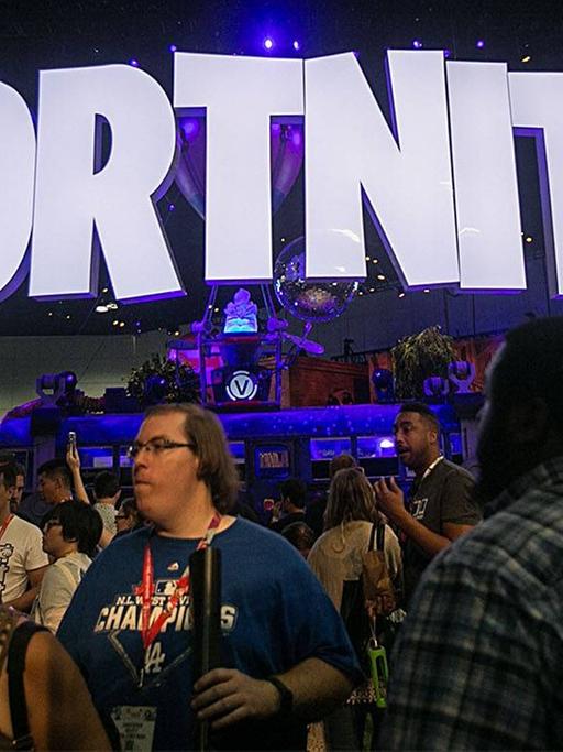 Verschiedene Leute stehen auf einem Messegelände unter einem Fortnite-Schild