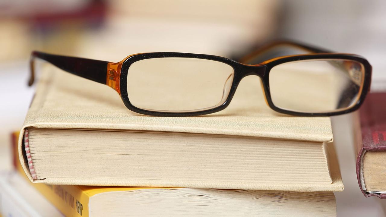 Eine Lesebrille liegt auf einem Bücherstapel. Eine Lesebrille liegt auf einem Bücherstapel.