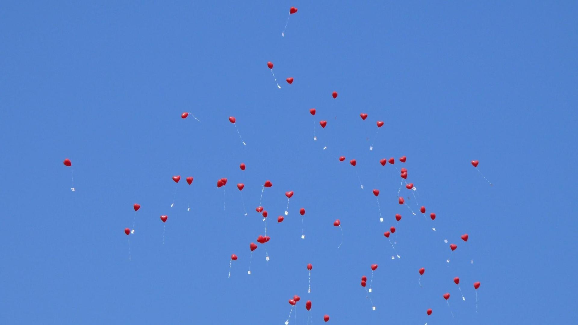 Fliegende rote Luftballons am blauen Himmel.